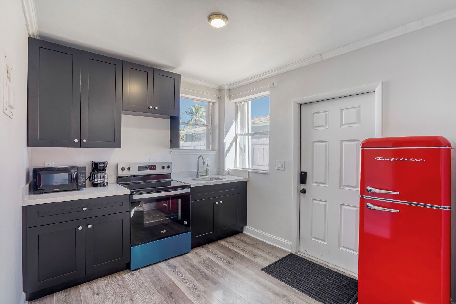 A modern kitchen with dark cabinets, a red refrigerator, and a built-in oven.