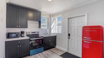 A modern kitchen with dark cabinets, a red refrigerator, and a built-in oven.