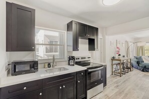 A modern kitchen with dark cabinetry, a built-in microwave, and a coffee maker. - Lauderdale Breeze Villas (Fort Lauderdale)