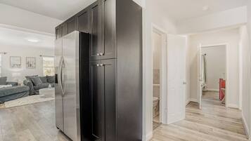 Una cocina moderna con refrigerador empotrado, un comedor con sofá y un pasillo que lleva a un baño.