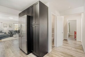 A modern kitchen with a built-in refrigerator, a dining area with a sofa, and a hallway leading to a bathroom. - Lauderdale Breeze Villas (Fort Lauderdale)