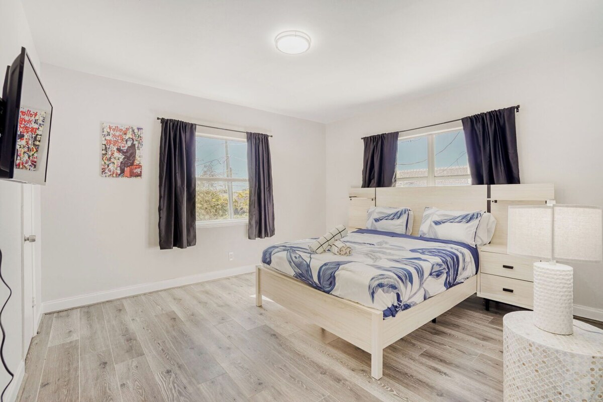 A bedroom with a bed, a bedside table, a lamp, and a window with curtains.