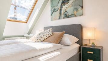 Ein Schlafzimmer mit Dachfenster, einem Bett mit weißer Bettwäsche, einem grauen Kopfteil und einem Nachttisch mit einer Lampe.