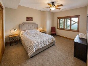 A bedroom with a bed, two bedside tables, a chair, a ceiling fan, a window, and a sign on the wall. - Kumbaya House: Steps from Cupp Run | Hot Tub, Deck & Epic Sunset Views (Snowshoe)