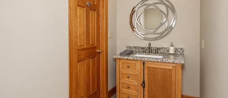A bathroom with a wooden door, a vanity with a sink, and a mirror above it.