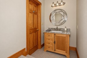 A bathroom with a wooden door, a vanity with a sink, and a mirror above it. - Kumbaya House: Steps from Cupp Run | Hot Tub, Deck & Epic Sunset Views (Snowshoe)