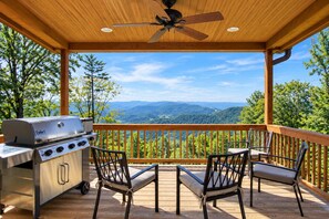 A covered outdoor area with a grill, two chairs, and a table, overlooking a mountainous landscape. - Kumbaya House: Steps from Cupp Run | Hot Tub, Deck & Epic Sunset Views (Snowshoe)
