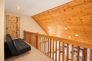 A modern interior with a wooden sloped ceiling, a black sofa, and a view of the outdoors. - Kumbaya House: Steps from Cupp Run | Hot Tub, Deck & Epic Sunset Views (Snowshoe)