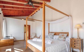 Ein Schlafzimmer mit Himmelbett, Holzboden, Deckenventilator, Nachttisch mit Lampe und einem zusätzlichen Beistelltisch.
