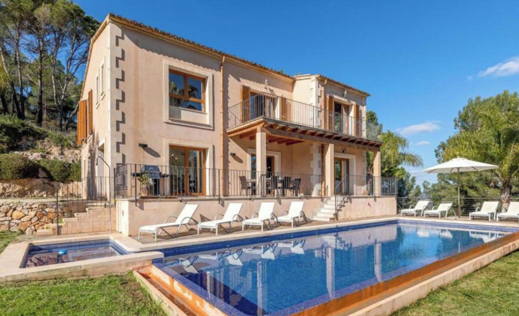 Une maison à deux étages avec une piscine, un espace salon extérieur et un mur en pierre.
