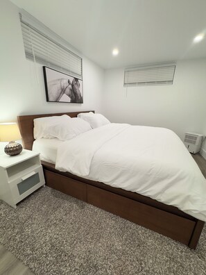Quarto com cama, mesa de cabeceira, luminária e quadro na parede.