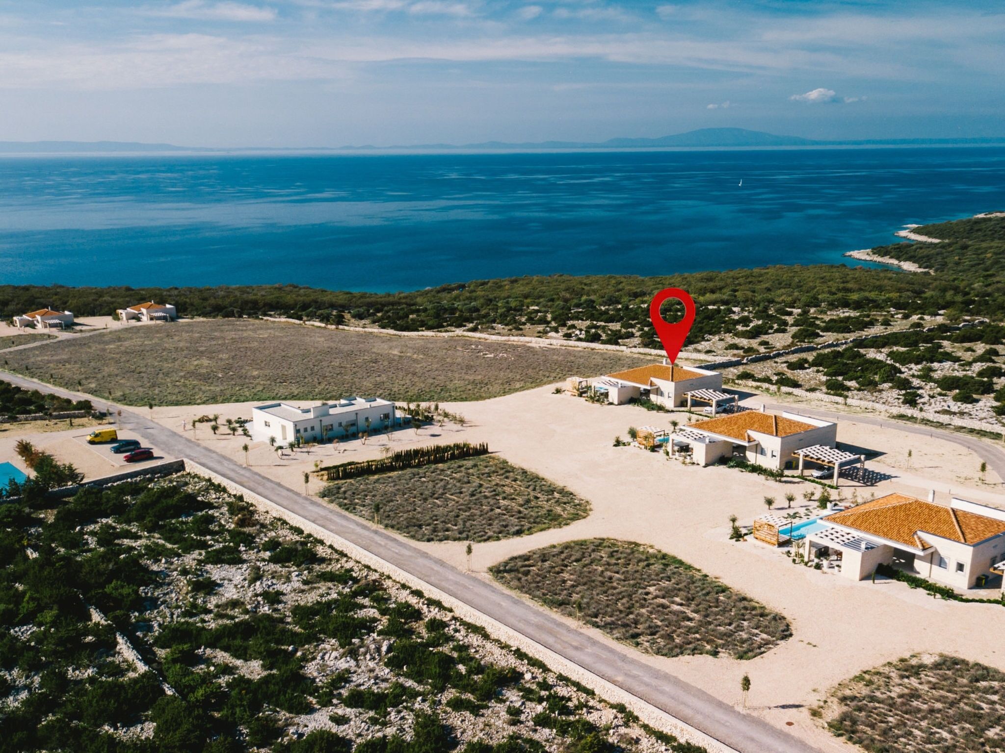 An aerial view of a coastal property with a swimming pool, a parking area, and a red location marker.