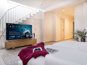 A modern living room with a flat-screen TV on a wooden stand, a white sofa, a staircase, and a door leading to another room. - 5* Luxury Seaview Villa Plant 3 with pool by Interhome (Novalja)