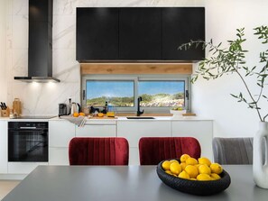 Une cuisine moderne dotée d’une grande fenêtre, d’une cuisinière encastrée et d’un coin repas avec une chaise rouge.