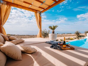 Un espace extérieur ensoleillé avec des sièges, offrant une vue sur la mer, une bouteille de champagne et un verre posé sur un plateau en bois.