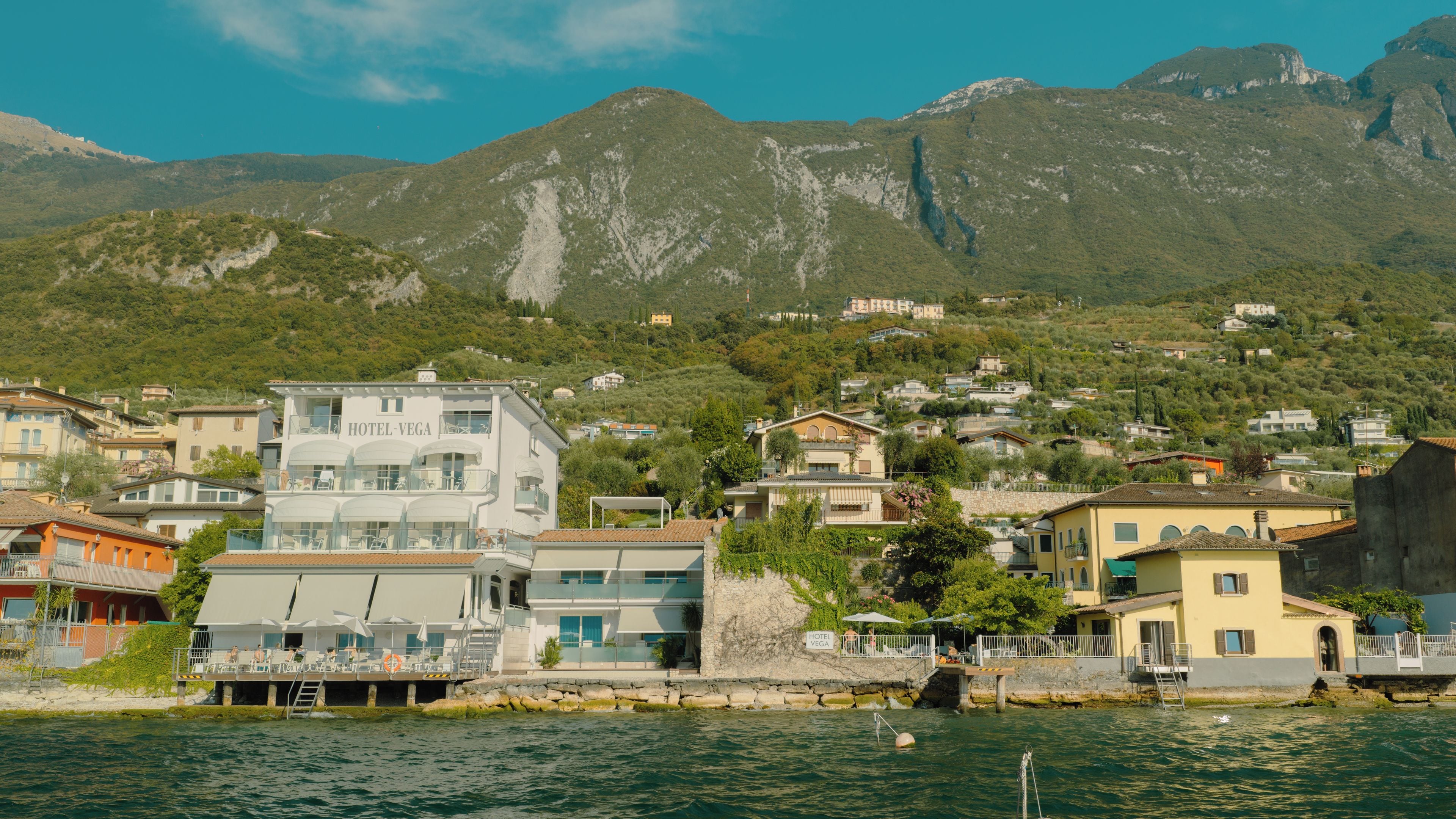 A coastal town with a prominent hotel named HOTEL-VEGA, featuring a modern building with balconies and a view of the sea.