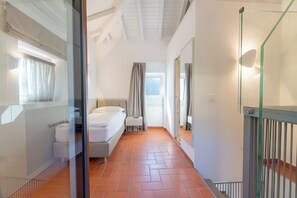 Een smalle gang met een bed, een klein tafeltje en een raam met gordijnen.