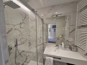 Un baño moderno con ducha envuelta en vidrio, un lavamanos blanco con espejo y una pared de mármol.