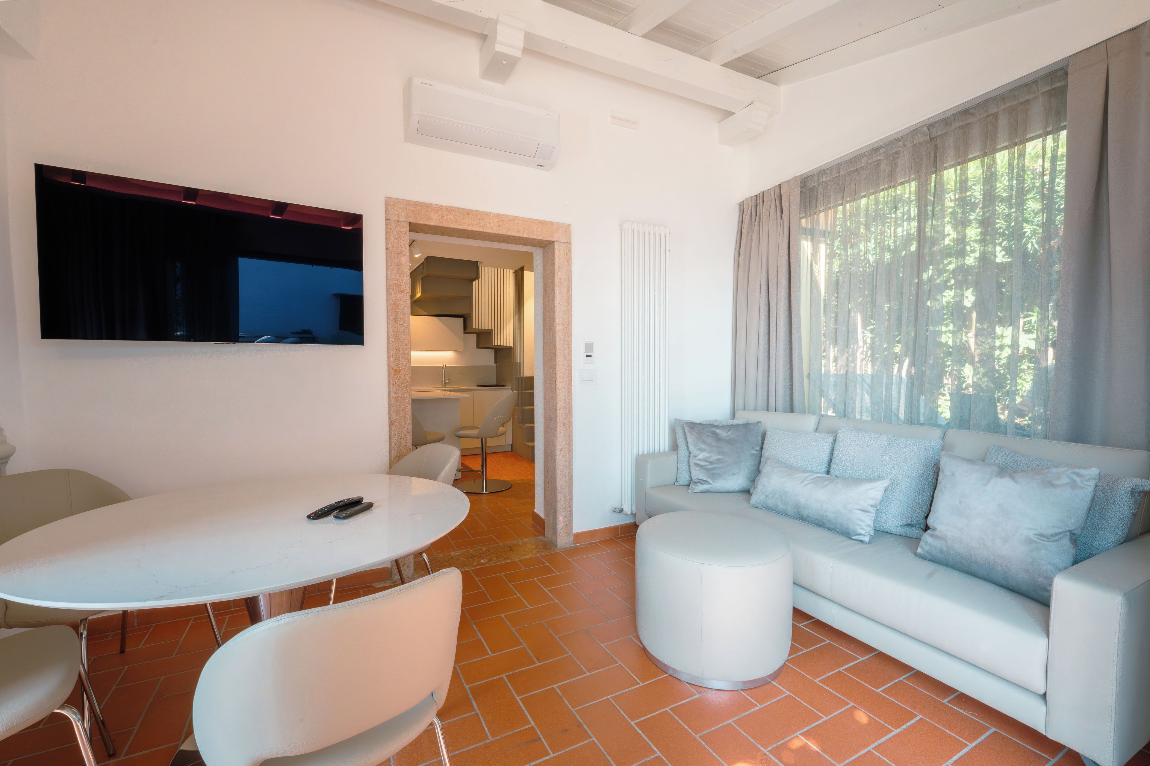 Ein modernes Wohnzimmer mit einem weißen Sofa, einem Esstisch und einem an der Wand montierten Fernseher.