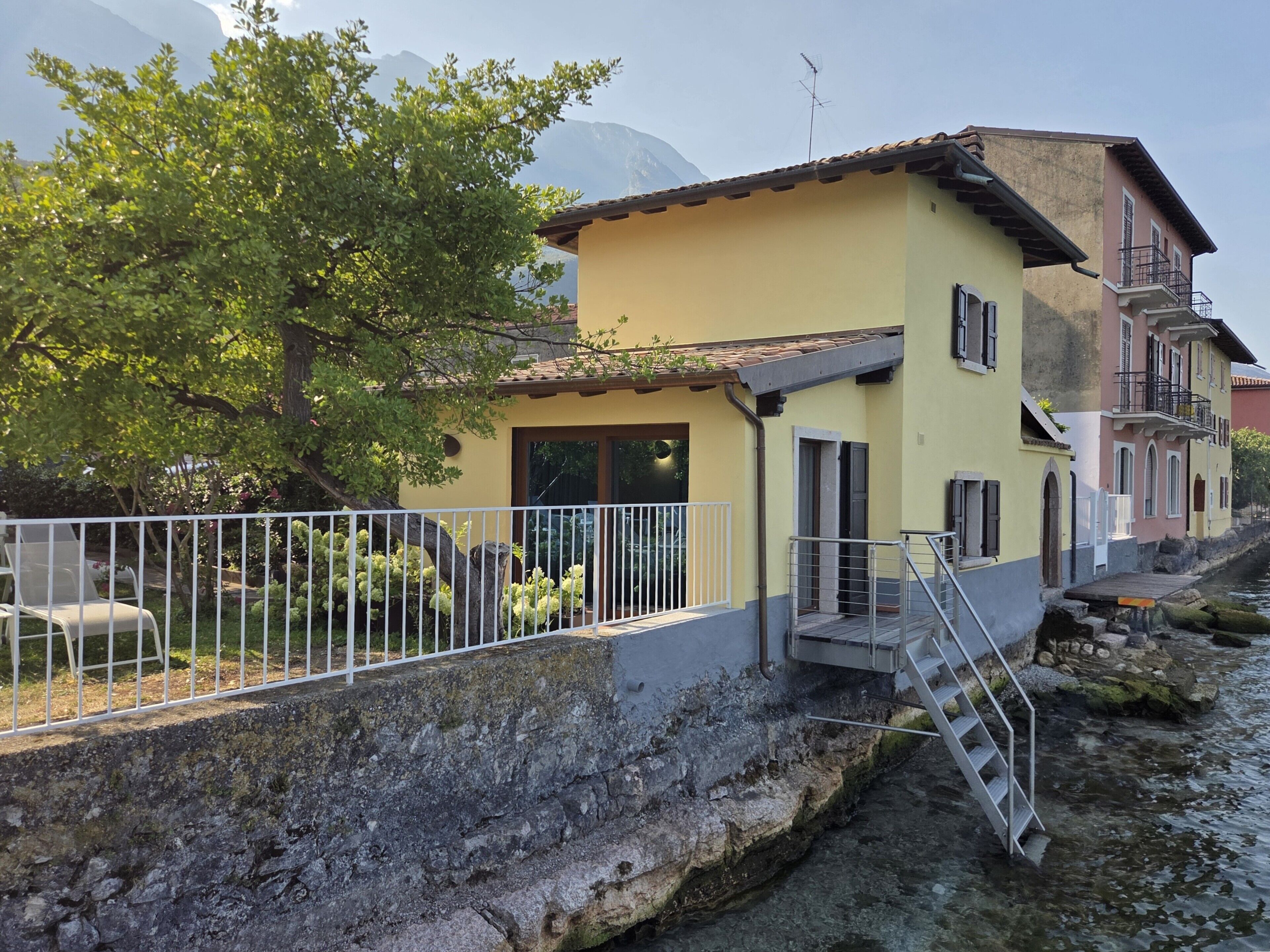 A yellow building with a balcony, a stone wall, and a river.