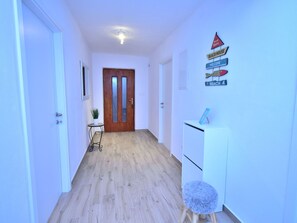 A hallway with wooden flooring, white walls, and a wooden door at the end. There are signs on the wall and a small table with a plant. - Holiday Home Dinko with pool by Interhome (Pridraga)
