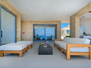 A modern living room with a large glass door leading to a balcony with a view of the sea. There are two sofas and a coffee table with a bottle and glasses on it. - 5* Luxury Seaview Villa Plant 6 with pool by Interhome (Novalja)