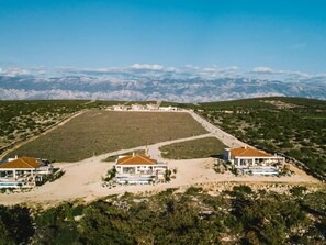 Una propietat costanera amb diversos edificis, un camp obert extens i un paisatge de muntanyes al fons.