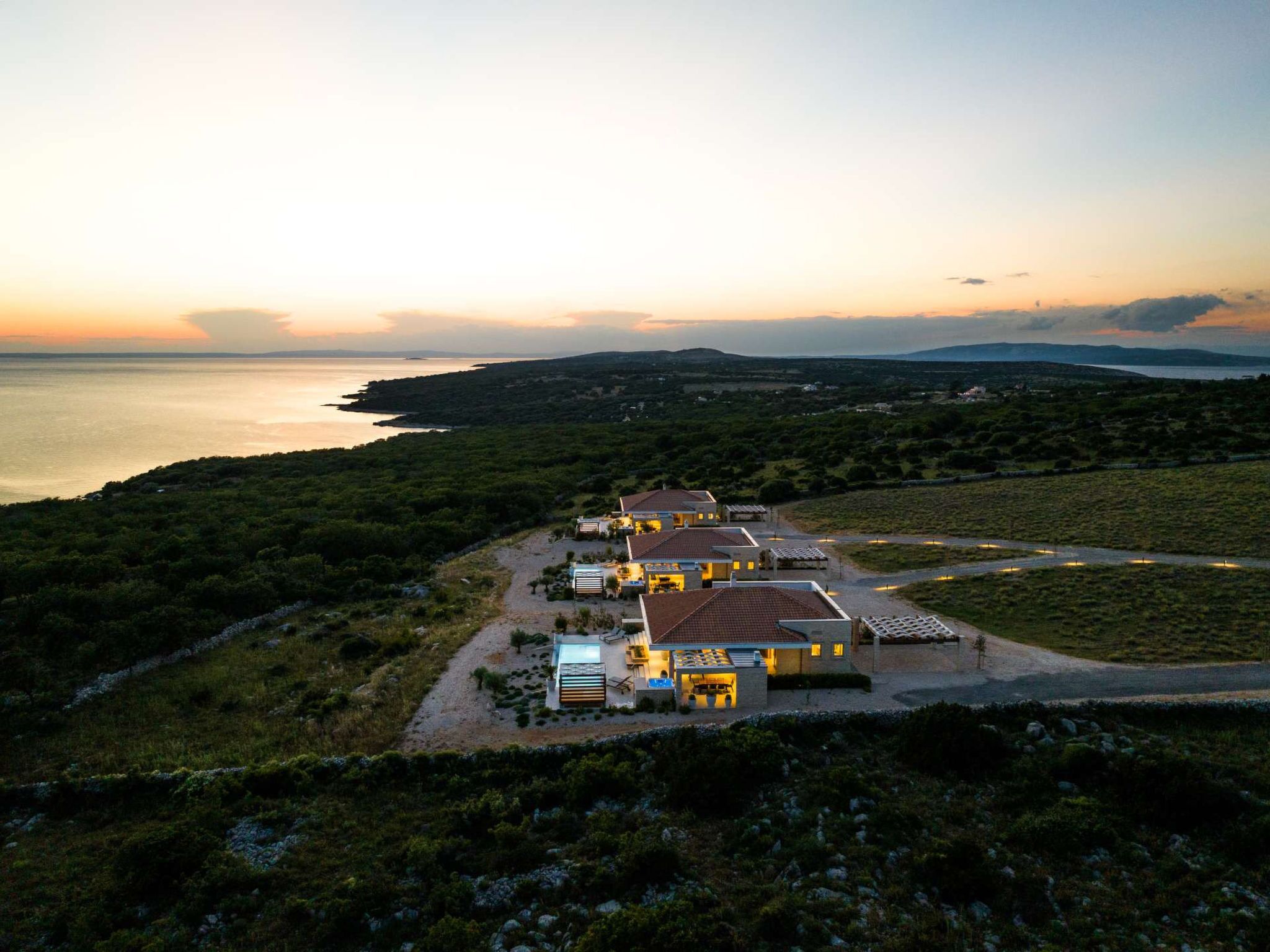 A coastal property with multiple buildings, a clear view of the sea, and a hilly landscape in the background.
