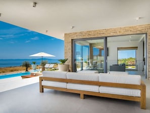 A modern outdoor living area with a pool, a wooden bench, and a view of the sea. - 5* Luxury Seaview Villa Plant 6 with pool by Interhome (Novalja)