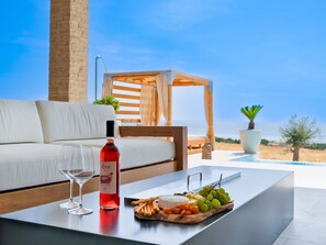 Ein moderner Außenbereich mit einer weißen Sitzecke, einer Holz-Pergola und einem Pool im Hintergrund.