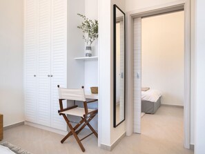 Een kamer met een witte garderobe, een tafeltje met een plant, een opklapbare stoel en een bed met een witte dekbedovertrek.