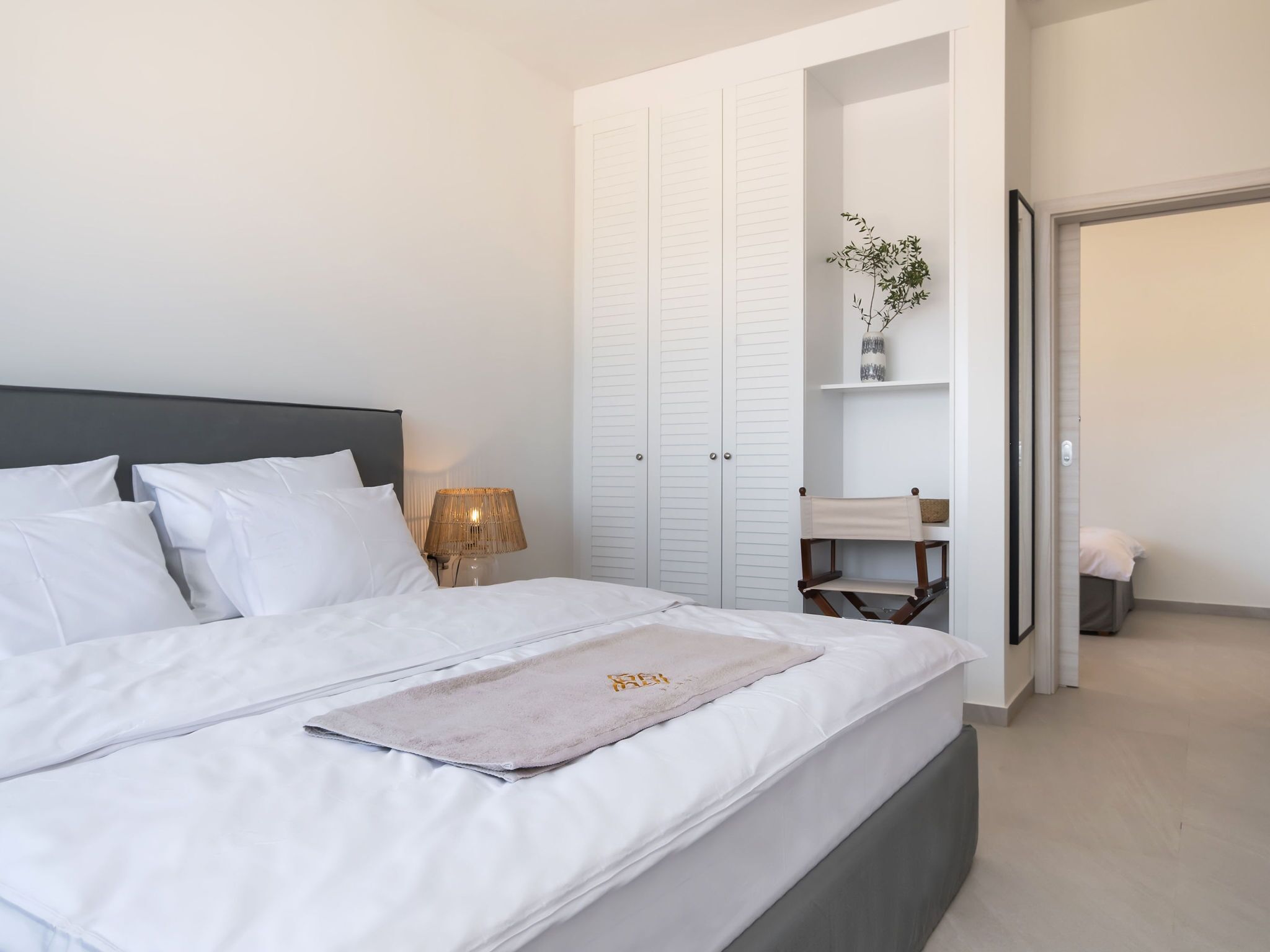 A neatly made bed with white linens, a bedside lamp, and a wardrobe with sliding doors.