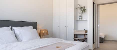 Un lit bien fait, avec du linge de lit blanc, une lampe de chevet et une armoire aux portes coulissantes.