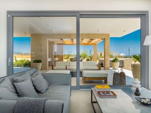 Un salon moderne avec un canapé gris, une table basse et une vue sur une terrasse extérieure aménagée avec des sièges et des plantes.