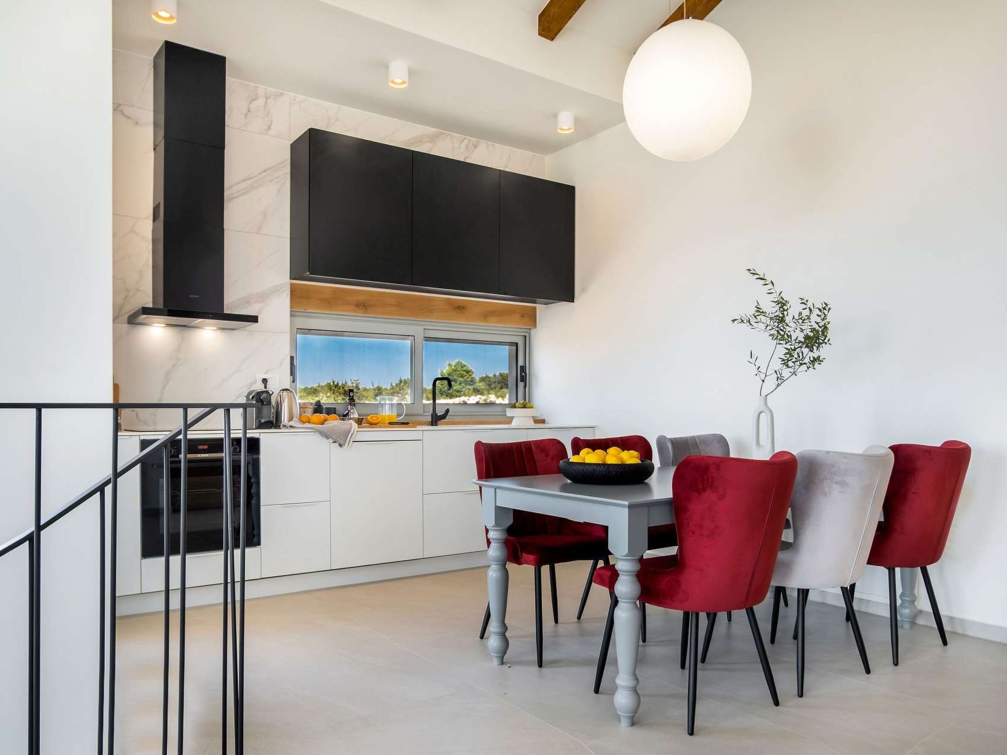 A modern kitchen with a dining area, featuring a marble countertop, black cabinets, and a view to the outdoors.