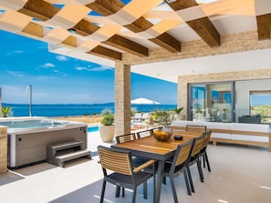 Eine Terrasss mit Whirlpool, Esstisch und Stühlen mit Blick auf einen Strand und das Meer.