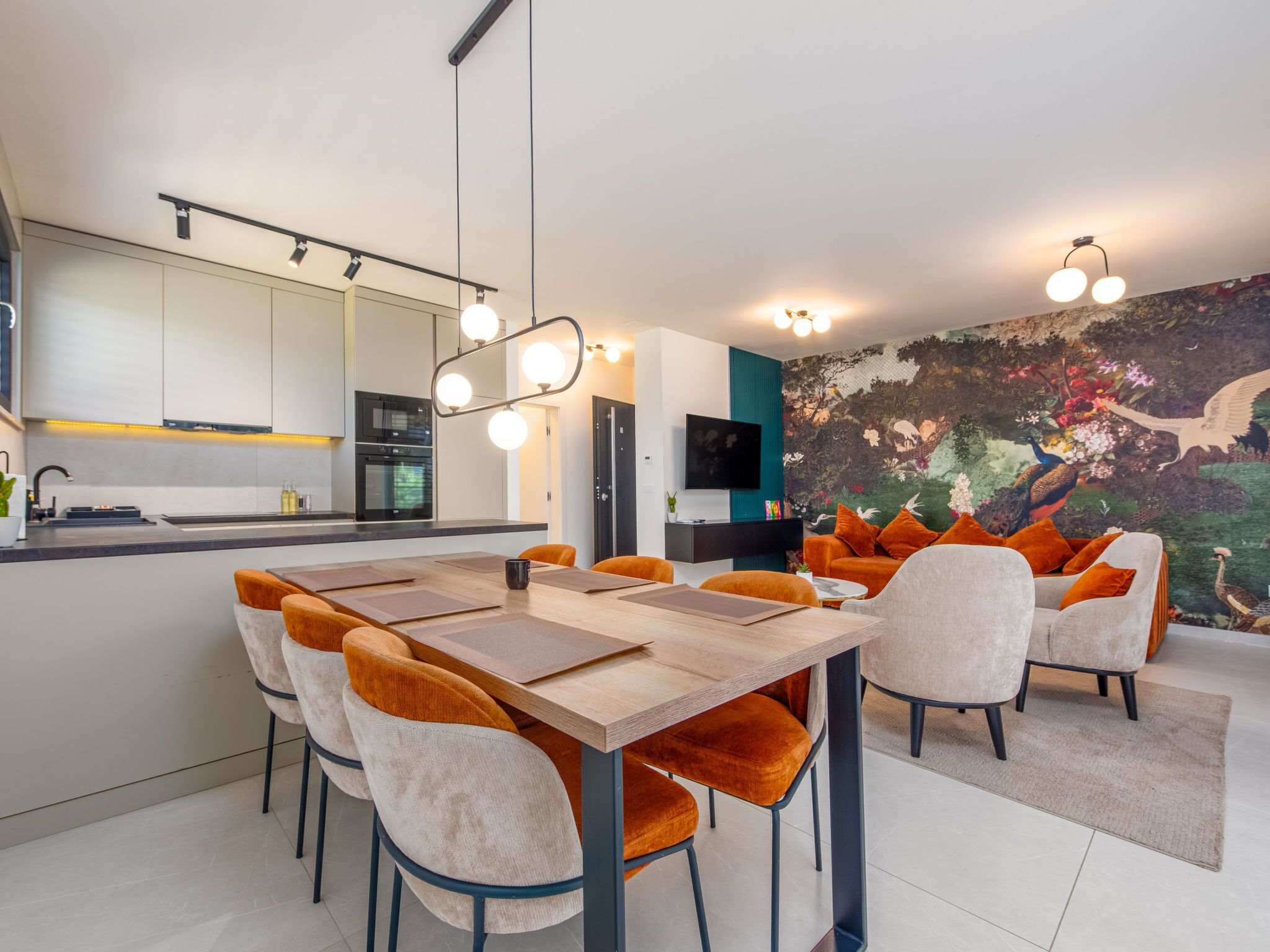 A modern kitchen with a dining area, featuring a large island, overhead lighting, and a vibrant mural.