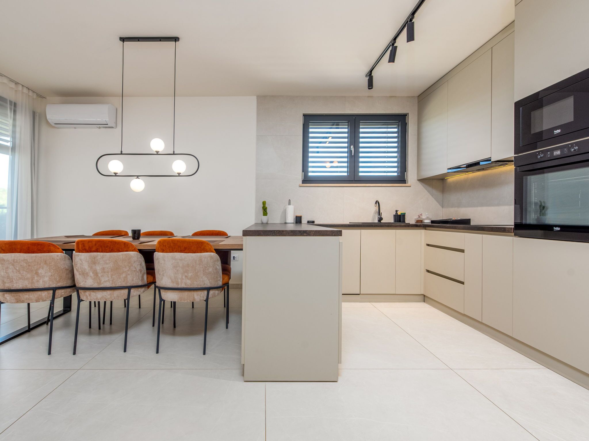 A modern kitchen with a central island, built-in appliances, and a dining area with chairs.