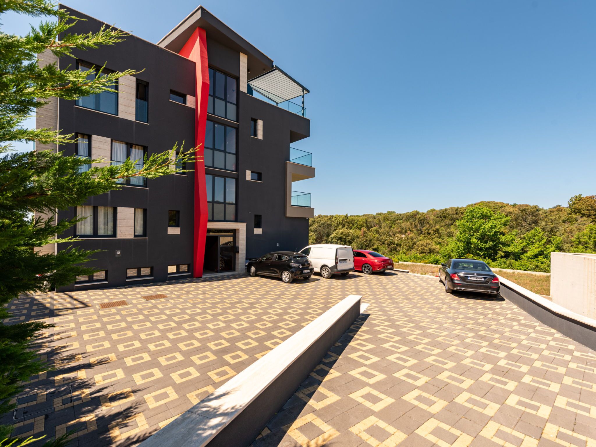 Een modern gebouw met rode accenten, een parkeerplaats en een heldere lucht.