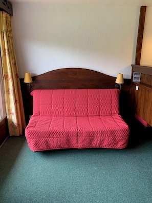 A red sofa with a wooden headboard in a room with teal carpeting.