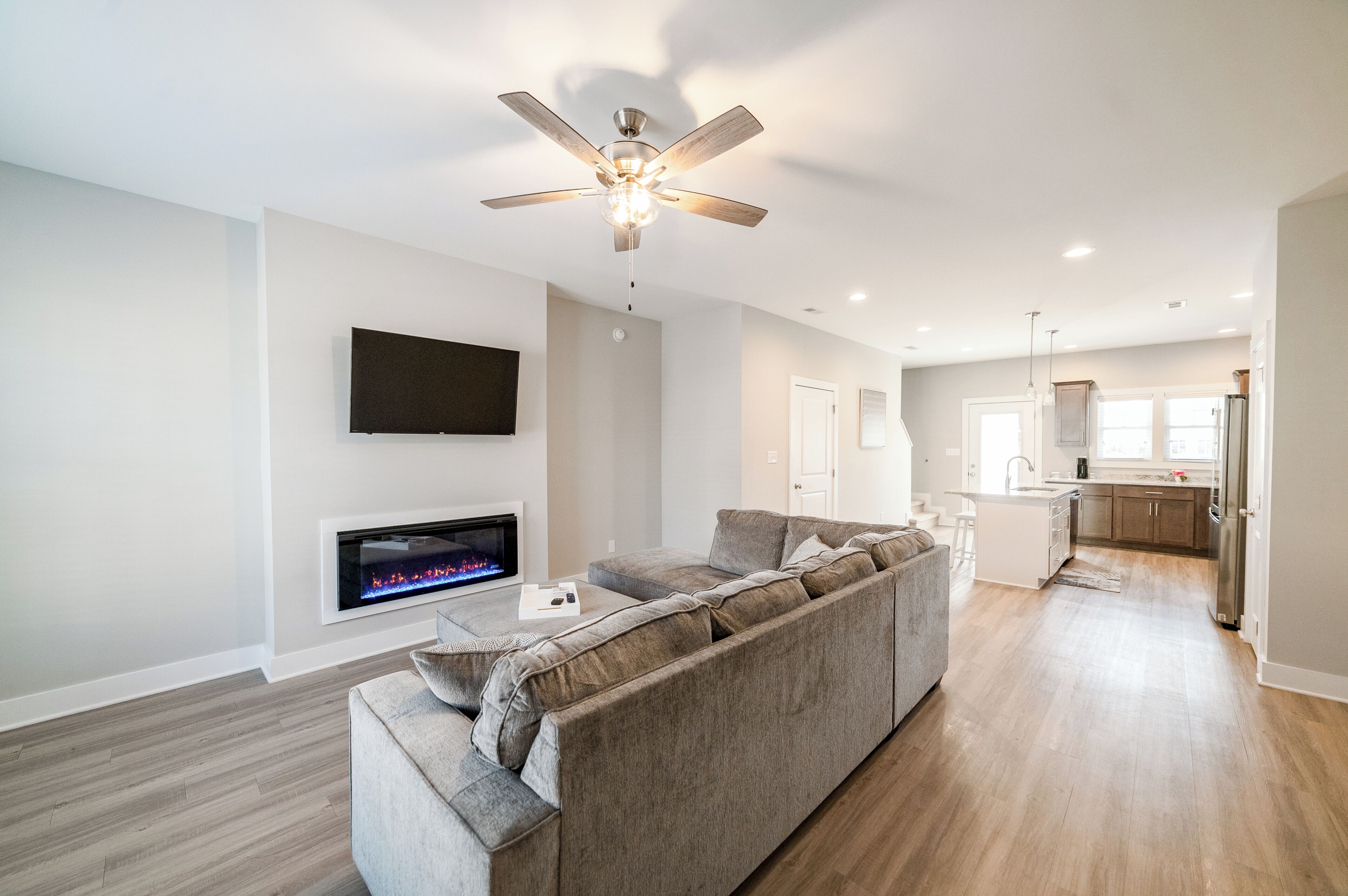 A modern living room with a sectional sofa, a flat-screen TV, a fireplace, and a ceiling fan.