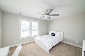 Ein Schlafzimmer mit einem Bett, einem Deckenventilator, einem Fenster und einem Teppichboden.