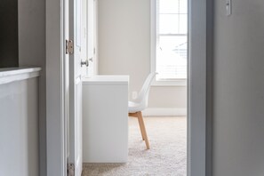 Een kamer met een witte garderobe, een witte stoel en een raam met zonwering.