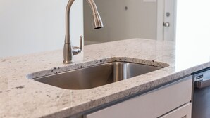 Una cocina con un lavamanos de acero inoxidable, encimera de granito y armario blanco.