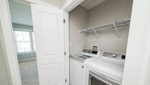 Un cuarto de lavandería con lavadora, secadora y un estante superior.