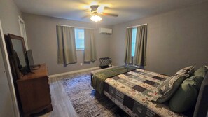 A bedroom with a bed, a dresser, a ceiling fan, and an air conditioning unit.