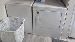 A laundry room with two stacked washing machines, a white laundry basket, and wooden cabinets above.