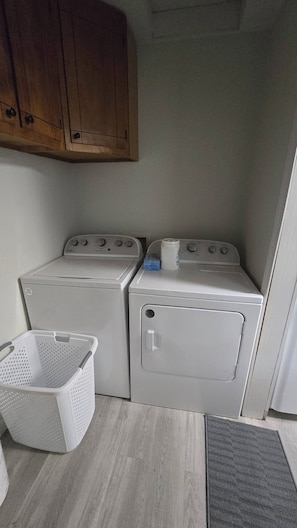 Un cuarto de lavandería con dos lavadoras apiladas, una cesta de ropa blanca y gabinetes de madera arriba.