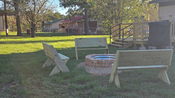 A wooden bench, a fire pit, and a wooden deck in a grassy outdoor area.