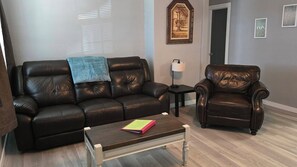 A living room with a dark brown leather sofa, a matching armchair, a small wooden coffee table, and a floor lamp.